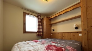 Een slaapkamer met een groot bed, een houten hoofdbord, twee bedlampen, een raam met gordijnen en een wandplank.