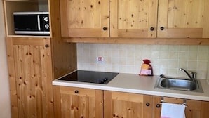 Een keuken met houten kastjes, een magnetron, een spoelbak en een wit aanrecht.
