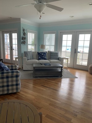 A living room with a white sofa, a grey ottoman, a checkered chair, a wooden table, and a ceiling fan.