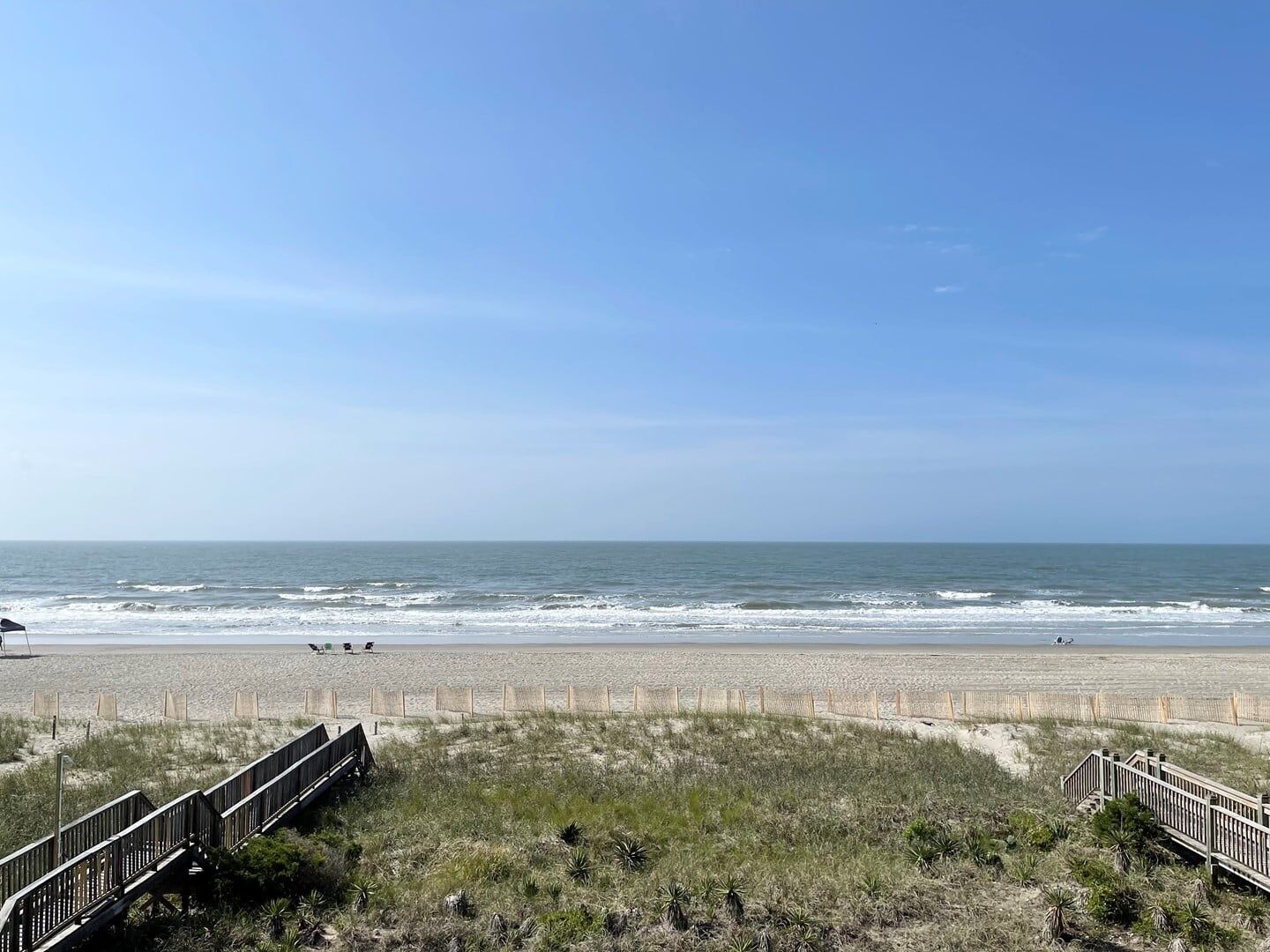 A beach with a wooden boardwalk leading to the shore, sandy dunes, and the ocean.