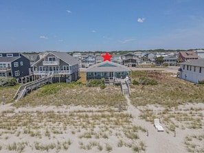 Uma área residencial costeira com casas, uma estrela vermelha em destaque em um edifício e uma praia de areia em primeiro plano.