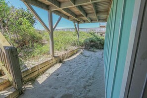 A covered outdoor area with a wooden deck and a sandy path leading to a wooden fence.
