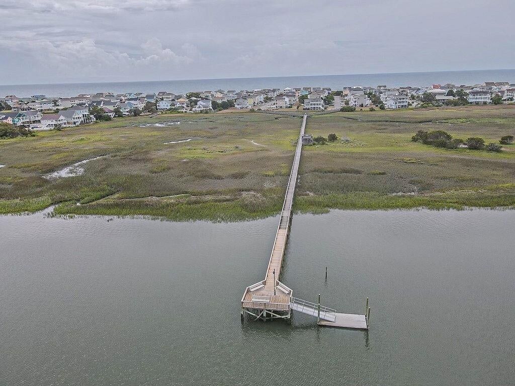 A long pier extending into a body of water with a residential area in the background.