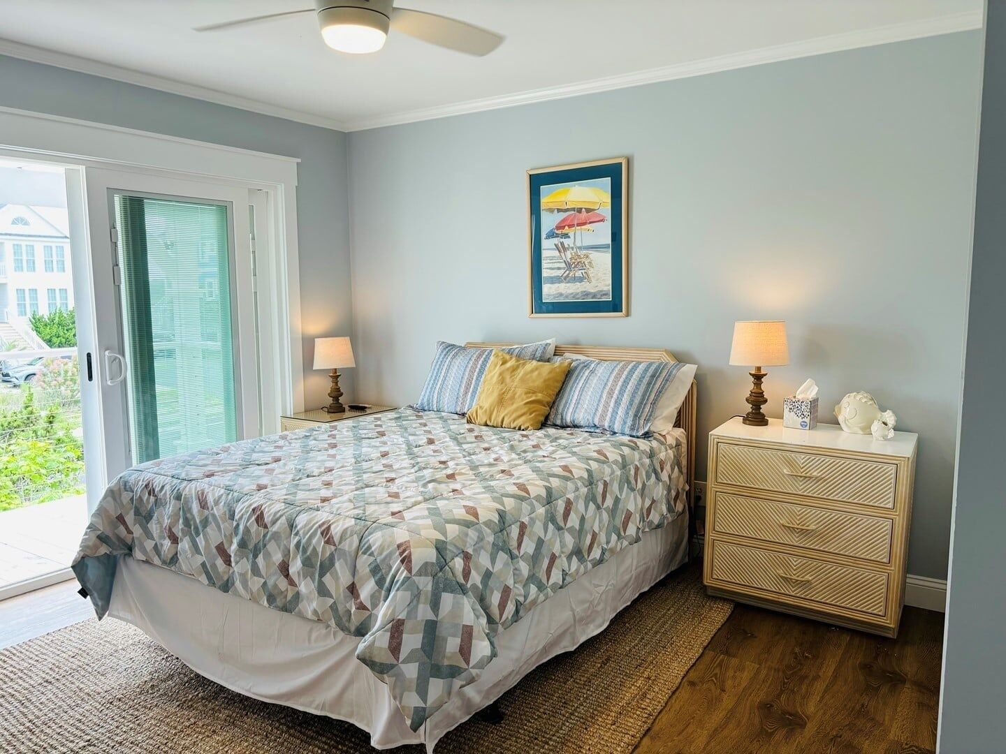 Een slaapkamer met een bed, twee nachtkastjes, een plafondventilator, een raam met zonwering en een lijst met een afbeelding aan de muur.