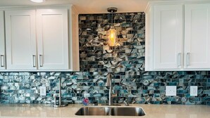 A kitchen with white cabinets, a stainless steel sink, and a backsplash with blue and white tiles.