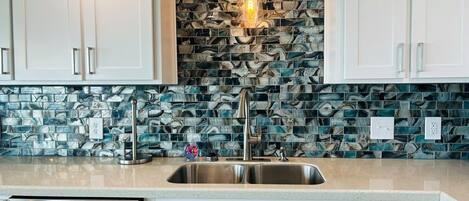 Cozinha com armários brancos, pia de aço inoxidável e backsplash com azulejos azuis e brancos.