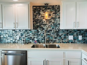 Una cocina con armarios blancos, un lavamanos de acero inoxidable y un salpicadero con azulejos azules y blancos.