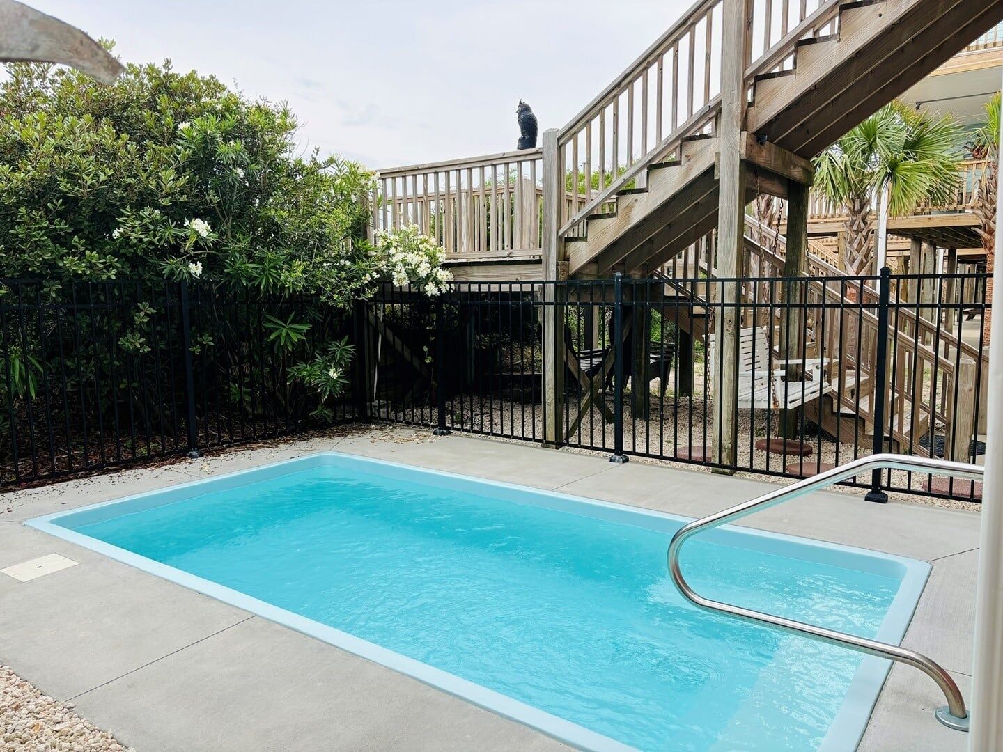 A rectangular pool with a metal ladder, surrounded by a wooden deck and a black metal fence.