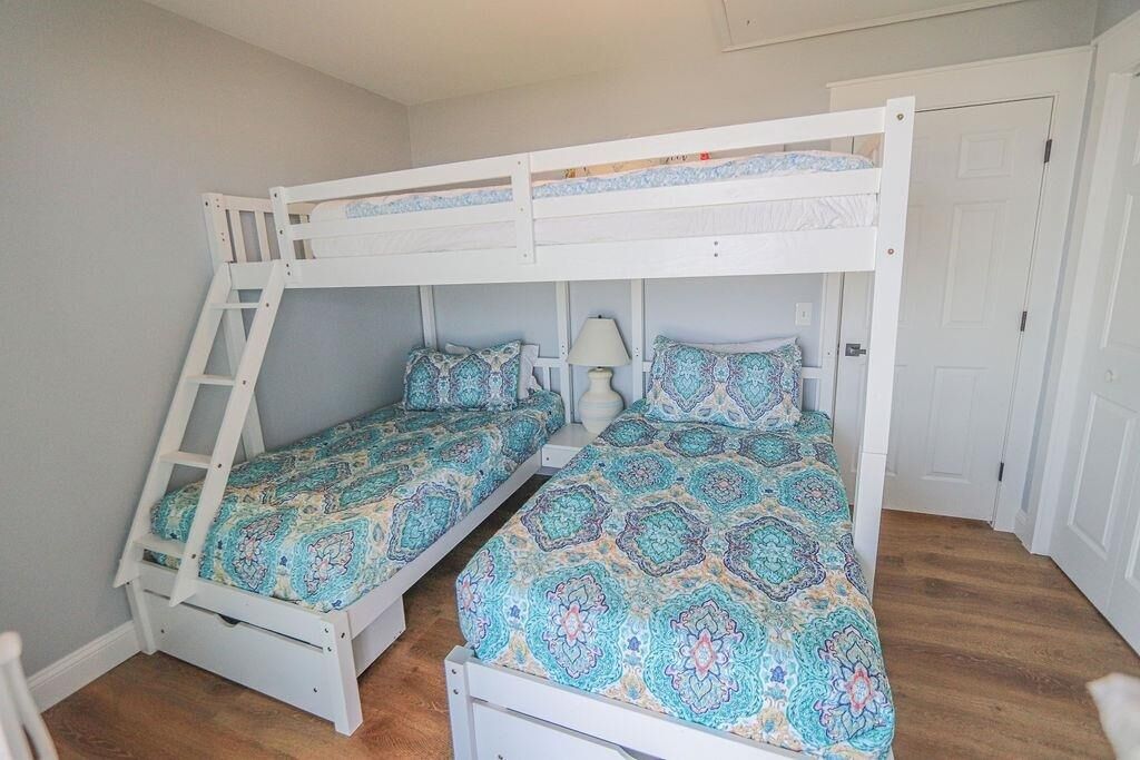 A room with two bunk beds, each with a ladder, a bedside table with a lamp, and patterned bedding.
