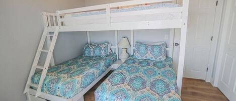 A room with two bunk beds, each with a ladder, a bedside table with a lamp, and patterned bedding.