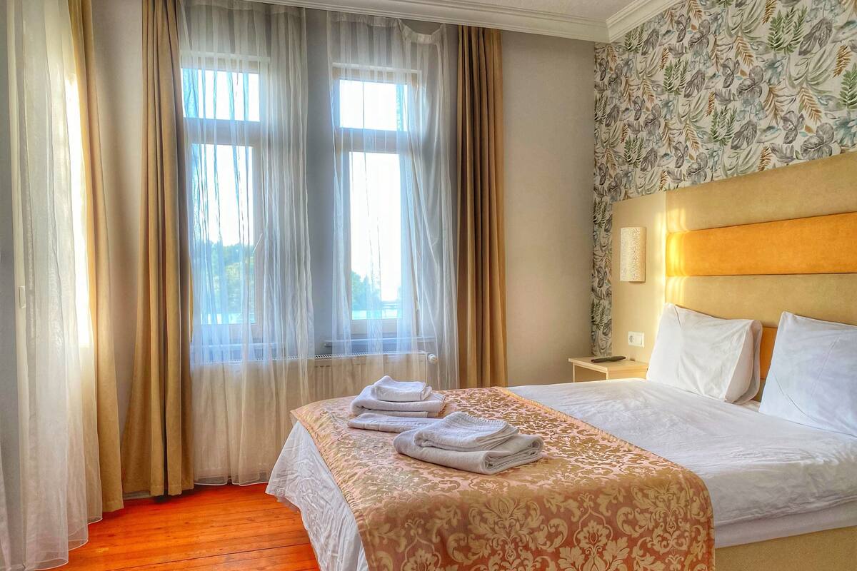 A hotel room with a bed, a nightstand, and a window with curtains.