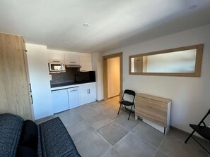 Eine moderne Küche mit weißen Schränken, einer Mikrowelle und einer schwarzen Arbeitsplatte. Im Raum befindet sich eine Holzbank und ein Stuhl.