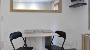 A room with a table set for two, a large mirror, a television mounted on the wall, and a small shelf.
