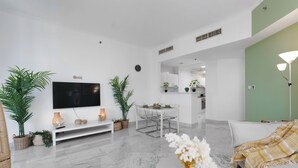 A modern living room with a flat-screen TV, a dining area, and a kitchen in the background. - Marco Polo - Stylish & Spacious 2 BR with Marina + City Views (Dubai)