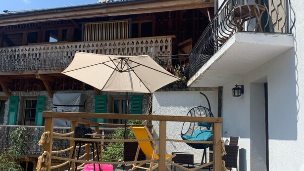 Una terraza de madera con barandilla de cuerda, mobiliario exterior y una silla colgante.