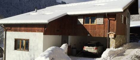 Een houten chalet met een sneeuwbedekte dak, een garage en een berg op de achtergrond.