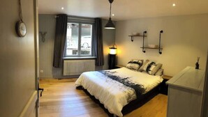 Un dormitorio con una cama grande, una ventana con cortinas, un radiador y una lámpara de noche.