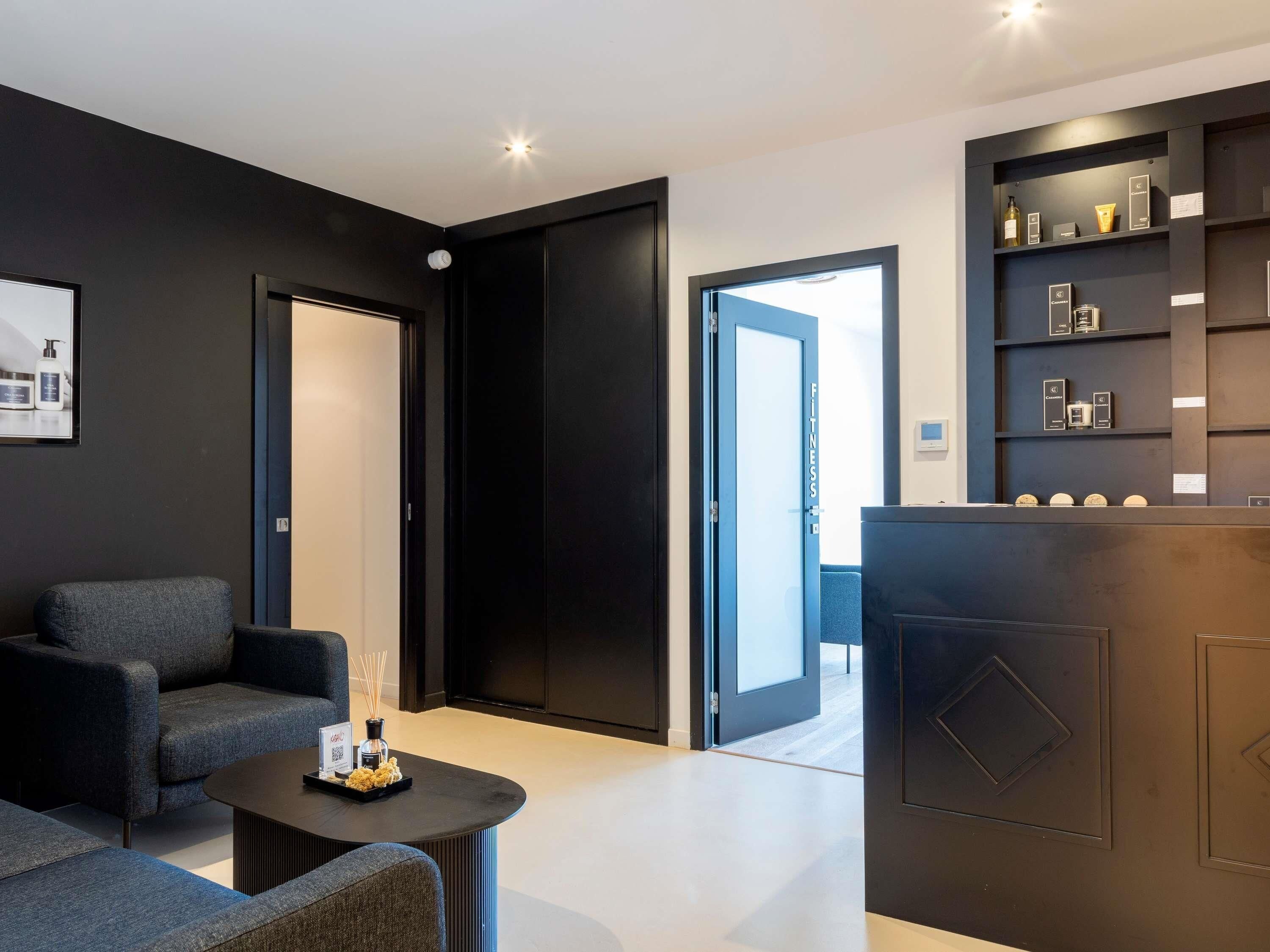 Un hall d’hôtel moderne avec un canapé, une table basse, un comptoir d’accueil et une porte donnant sur un balcon.