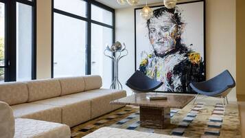 A modern living room with a beige sofa, a coffee table, and two blue chairs. There is a large abstract painting on the wall and a floor lamp.