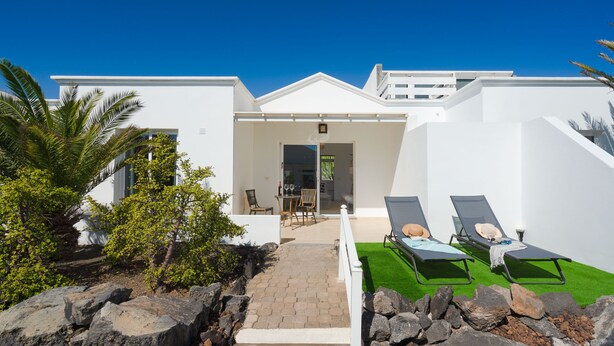 A modern white building with a patio area featuring two lounge chairs and a small table. - Luxurious A2 in a small complex with communal pool 100m from the sea (Charco del Palo)