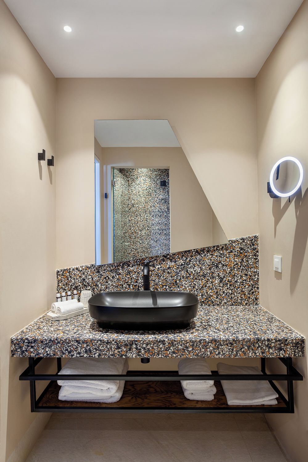 A modern bathroom with a black sink, a speckled countertop, and a mirror with a light.