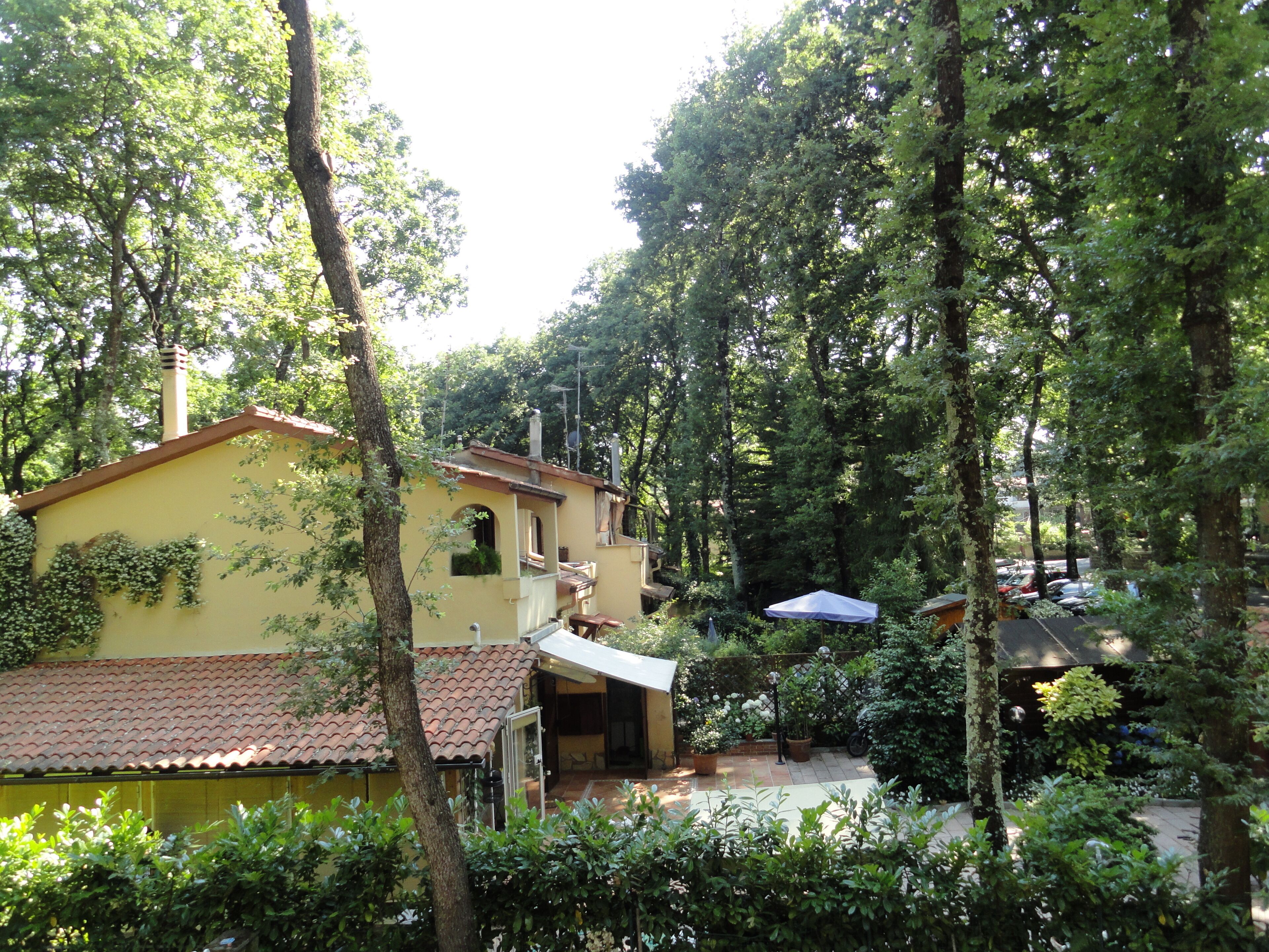 A yellow building with a tiled roof, surrounded by trees and a garden area.
