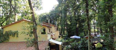 A yellow building with a tiled roof, surrounded by trees and a garden area.
