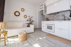 A modern kitchen with white cabinets, a tiled backsplash, and a built-in oven. There is a white sofa with cushions and a wicker basket on the floor.