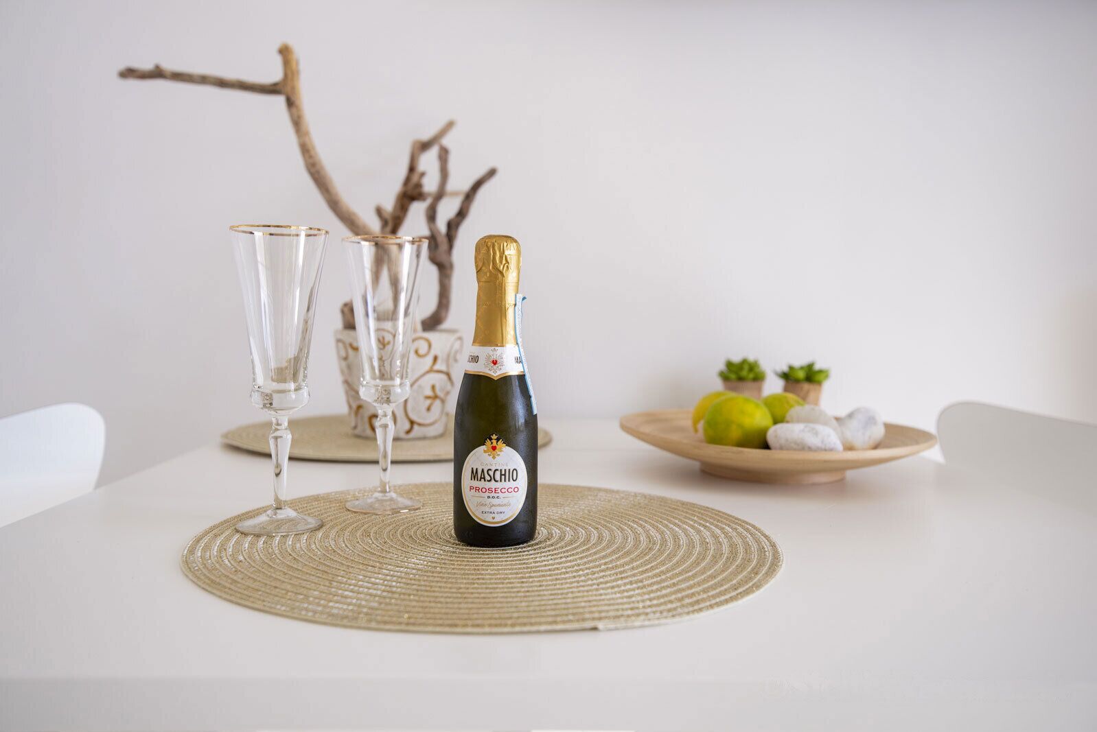 Eine Flasche Maschio Prosecco auf einem Tisch mit zwei Gläsern und einer Obstplatte.