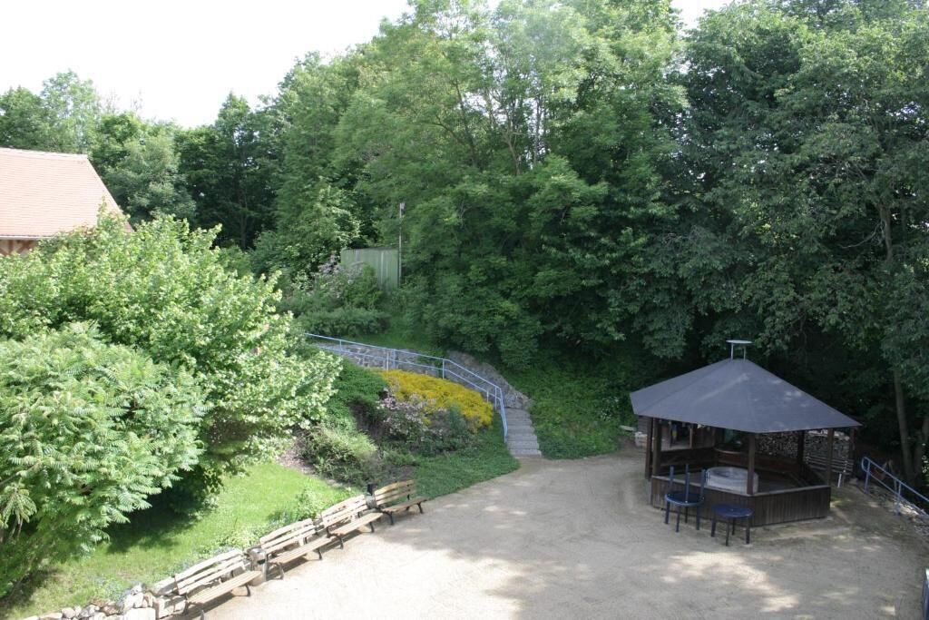 A gazebo with a roof and seating, surrounded by a dirt path and greenery.