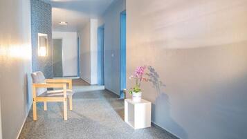 Un pasillo con una silla de madera, una mesita auxiliar blanca con planta en maceta y un espejo en la pared.