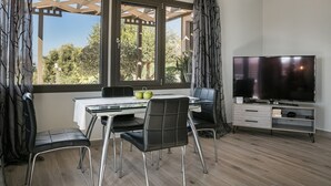 A modern living room with a glass dining table, black chairs, a flat-screen TV, and a wooden floor. - Villa Mariliza, ιδανική επιλογή για να αποδρά... (Argostoli)
