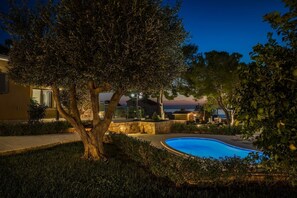 A swimming pool surrounded by trees and a stone wall, with a building in the background.