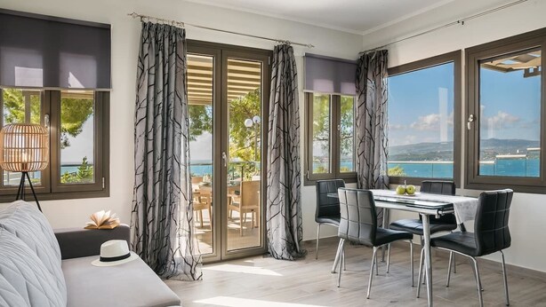 A modern living room with a sofa, a dining table with chairs, and large windows offering a view of the sea. - Villa Mariliza, ιδανική επιλο γή για να αποδρά... (Argostoli)