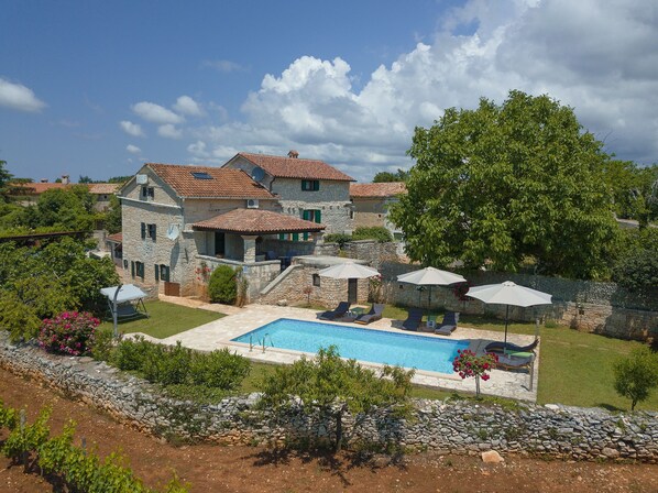 Uma vila de pedra com piscina, área de estar externa e vegetação exuberante.