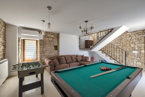 Quarto com mesa de bilhar, mesa de futebol de mesa e escadaria com paredes de pedra.