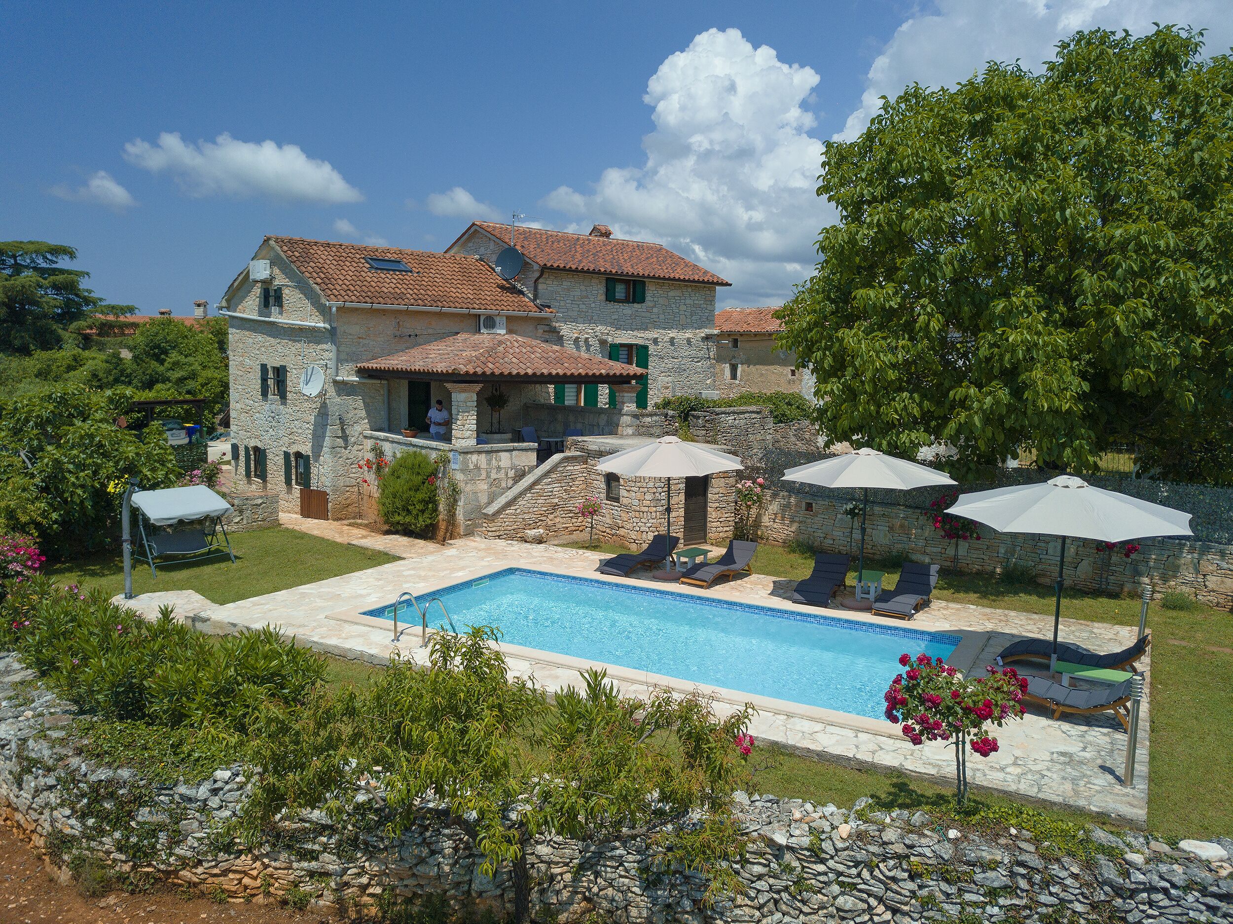 A stone villa with a swimming pool, outdoor seating, and lush greenery.
