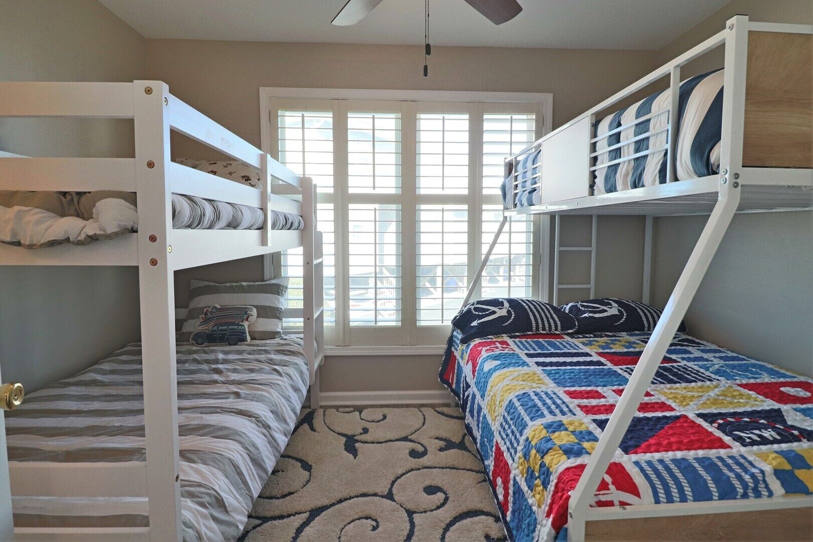 A bunk bed room with a window, a patterned rug, and a quilted bedspread.