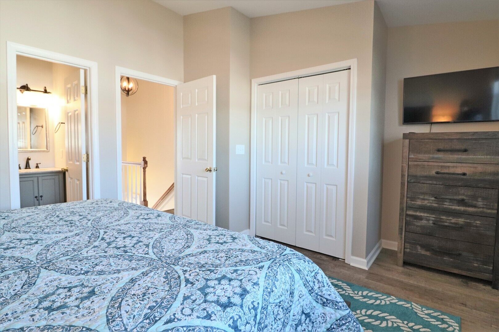 Une chambre avec un grand lit, une commode, un téléviseur et deux portes.