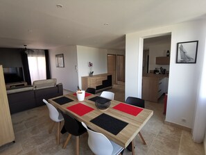 Una sala de estar moderna con comedor, televisor y cocina al fondo.