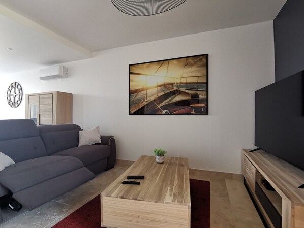A modern living room with a grey sofa, a wooden coffee table, a TV stand, and a wall-mounted picture of a boat.