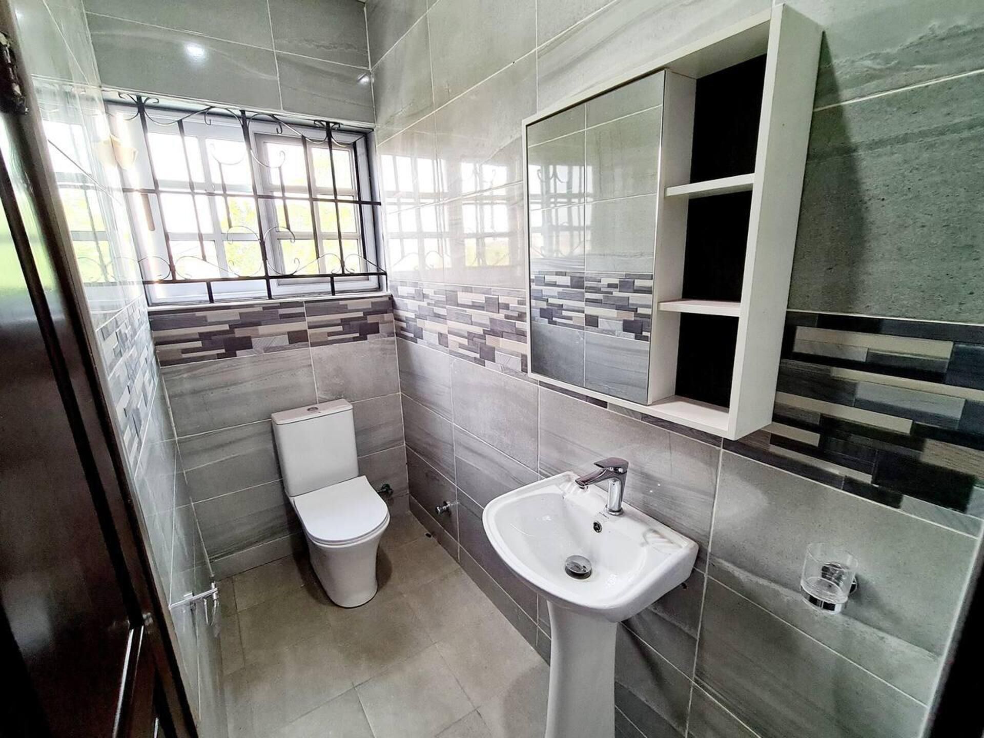 Een moderne badkamer met toilet, wastafel en een raam met tralies.