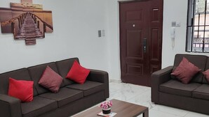 A living room with two dark brown sofas, each with red cushions, a wooden coffee table with a vase of flowers, and a large wooden artwork above the sofa. - Cozy,quiet & Fantastic- Close to Highway - Parking (Adenta)