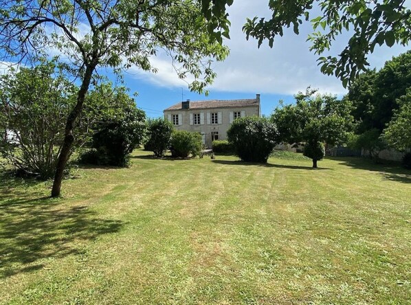 Uma casa grande de dois andares, com um gramado bem cuidado e várias árvores.