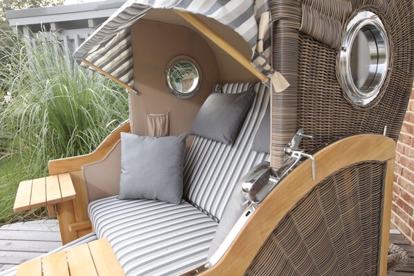 A cozy outdoor seating area with a cushioned bench, a small table, and a wicker wall structure.