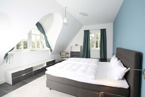 Une chambre moderne avec un grand lit, une banquette intégrée et une fenêtre avec des rideaux.