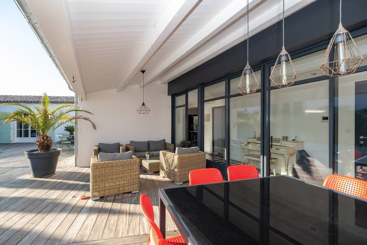 Un espace extérieur aménagé en terrasse, avec des meubles en osier, une table en verre et des lampes suspendues.