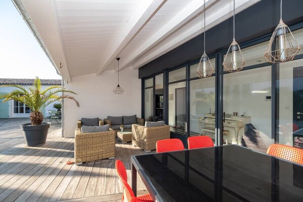 Un espacio al aire libre con patio, mobiliario de mimbre, una mesa de vidrio y lámparas colgantes.