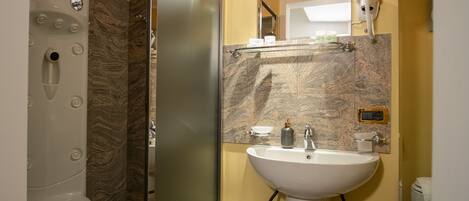 Un baño moderno con ducha de vidrio, lavamanos blanco y salpicadero de mármol.