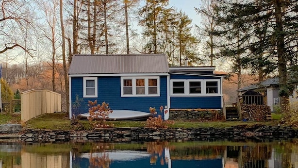 Une maison bleue avec un étang devant, entourée d’arbres.